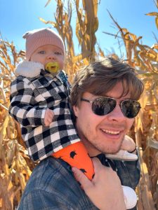 Bill Davis holding a baby in front of a corn field.