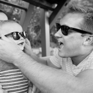 Joe Rasmussen wearing sunglasses puts a pair of sunglasses on a child.