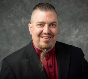 Timothy Bohn with a beard wearing a suit and tie.