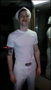 Aaron Goodwin in a white t-shirt, white pants, and a sailor hat.