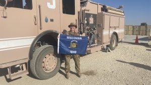 Abygail Boyle holding a State of Wisconsin flag in front of a military fire truck.