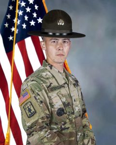 Alvin Osterndorff in uniform and a drill sergeant hat with a flag behind him.