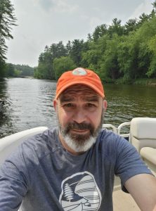 Craig Boehlke wearing an orange hat on a boat with trees in the background.