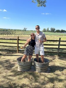 Colin Kenny and a woman posing for a picture at a winery holding wine glasses.