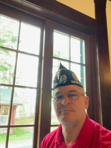 Darral AJ Feucht takes a selfie wearing a red collared shirt and black and yellow Garrison cap.