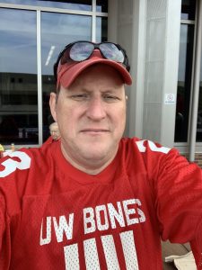David Hanson takes a selfie in a red baseball hat, sunglasses, and a red jersey labelled "UW Bones"