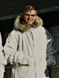 Dennis Carlson poses for a photo outside in direct sunlight, squinting and wearing a large light gray winter coat.