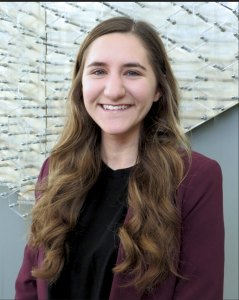 Hannah Schuh poses for a headshot in a maroon blazer and black shirt, smiling.