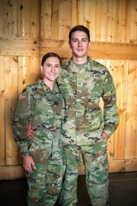 Hannah Schuh in her Army uniform next to another man in uniform post against a wooden wall.