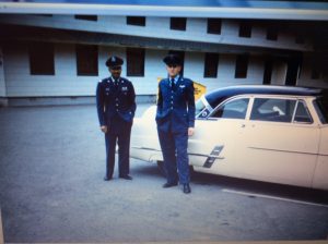 James Meinberg and another soldier stand in uniform next to a yellow car.