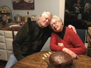 James Meinberg hugs another individual in front of a chocolate cake with candles on it.