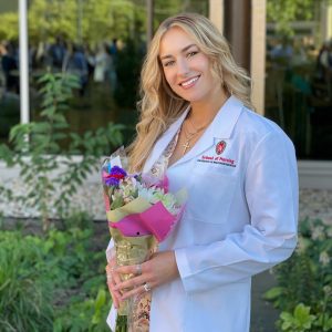 Mira Tcherneva is wearing a white School of Nursing coat holding a bouquet of flowers.