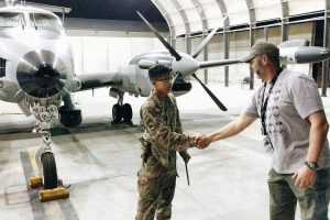 Miguel Pingol is in uniform shaking someone's hand in front of an airplane inside a hangar.