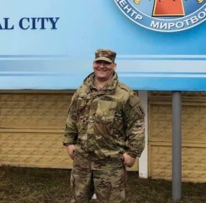 Nathan Weier in uniform poses for a picture outside in front of a sign in Russian.