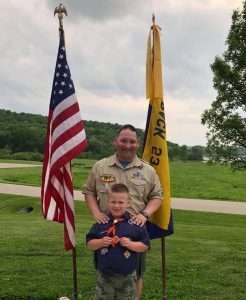 Nathan Weier and a younger child in their Boy Scouts uniforms stand outside in front of an American flag.