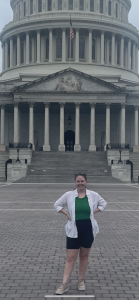 Rita Stull poses in front of the Capitol building in shorts and a white button up with a green shirt underneath.