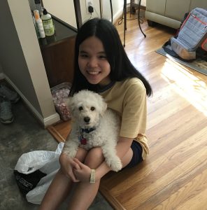 Thi Tran smiles for a photo sitting on the floor holding a small white dog.