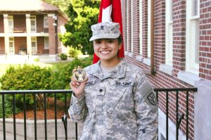 Ana Maria Moyer in uniform holding a medal outside by a brick wall and trees.
