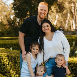 Ana Maria Moyer with her husband and three children smiling for a photo outside with plants in the background.