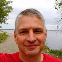 Brian Kline smiling in a selfie wearing a red shirt with nature in the background.