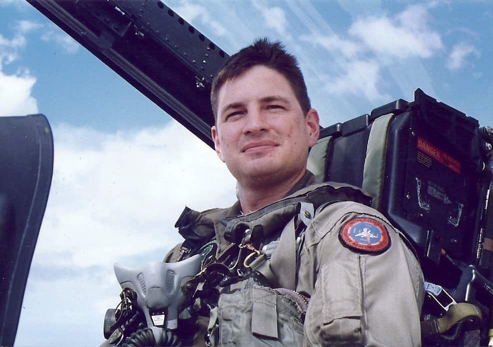Brian Kline in uniform inside a fighter jet with clouds in the background.