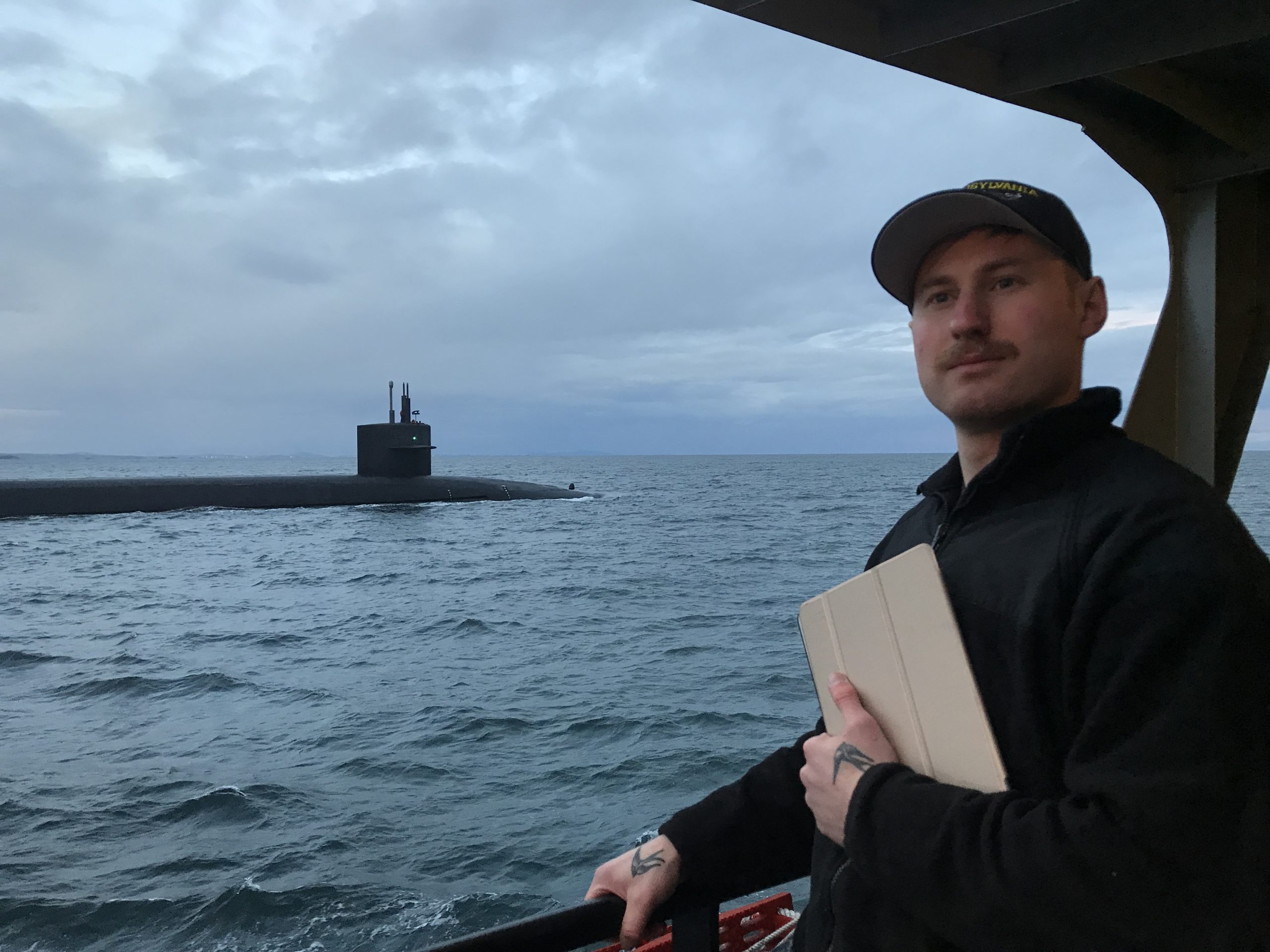Andrew Ledoux holding an iPad with a body of water and submarine in the background.
