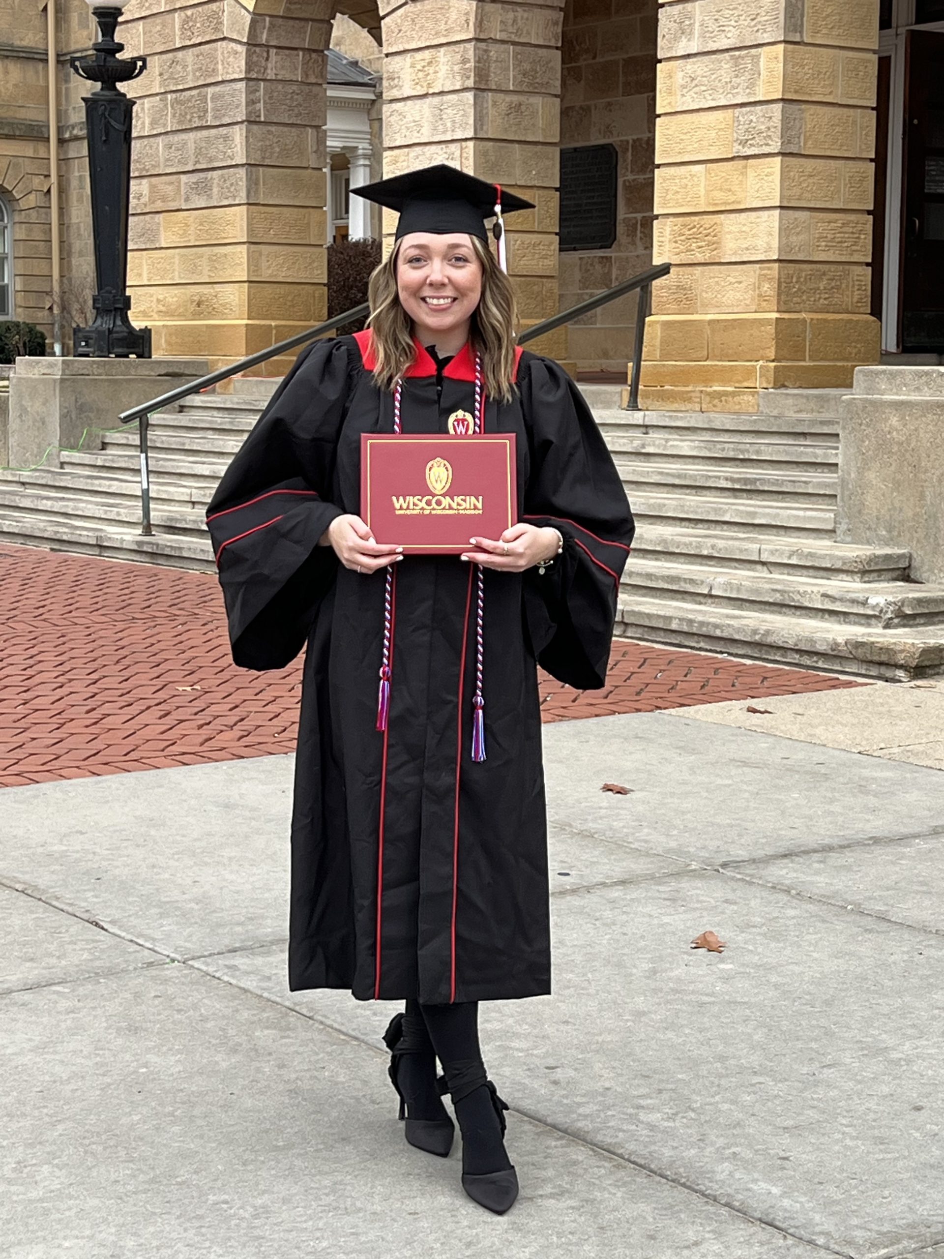 Eliza Rushlow in a graduation cap and gown with a diploma smiling for a photo.