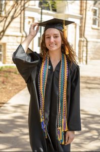 Ruthie Zahm in a graduation cap and gown smiling for a photo outside.