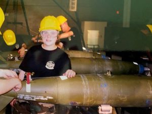 Maggie Zabinski working on a missile while wearing a yellow hard hat and black t-shirt.
