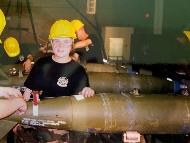 Maggie Zabinski working on a missile while wearing a yellow hard hat and black t-shirt.