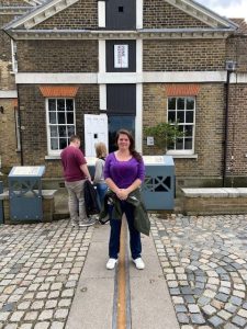 Maggie Zabinski wearing a purple shirt and jeans standing in front of a brick house.