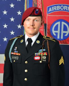 Owen Olichwier in uniform smiling for a photo with the American flag in the background.