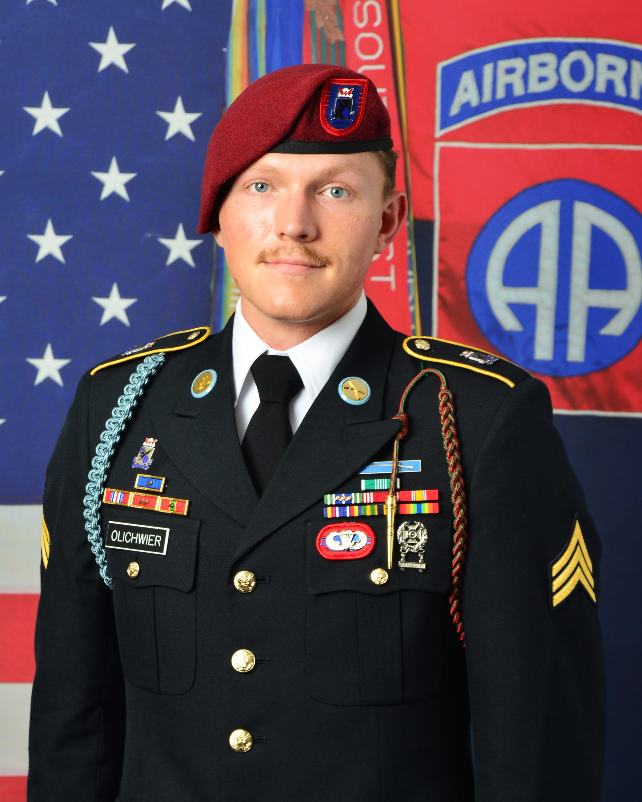 Owen Olichwier in uniform smiling for a photo with the American flag in the background.