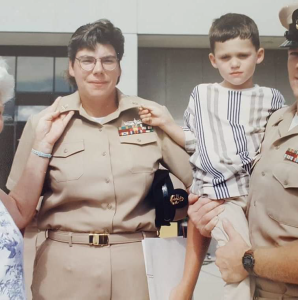 Lorraine Schwager in tan uniform smiling for a photo with a young child and man in uniform.
