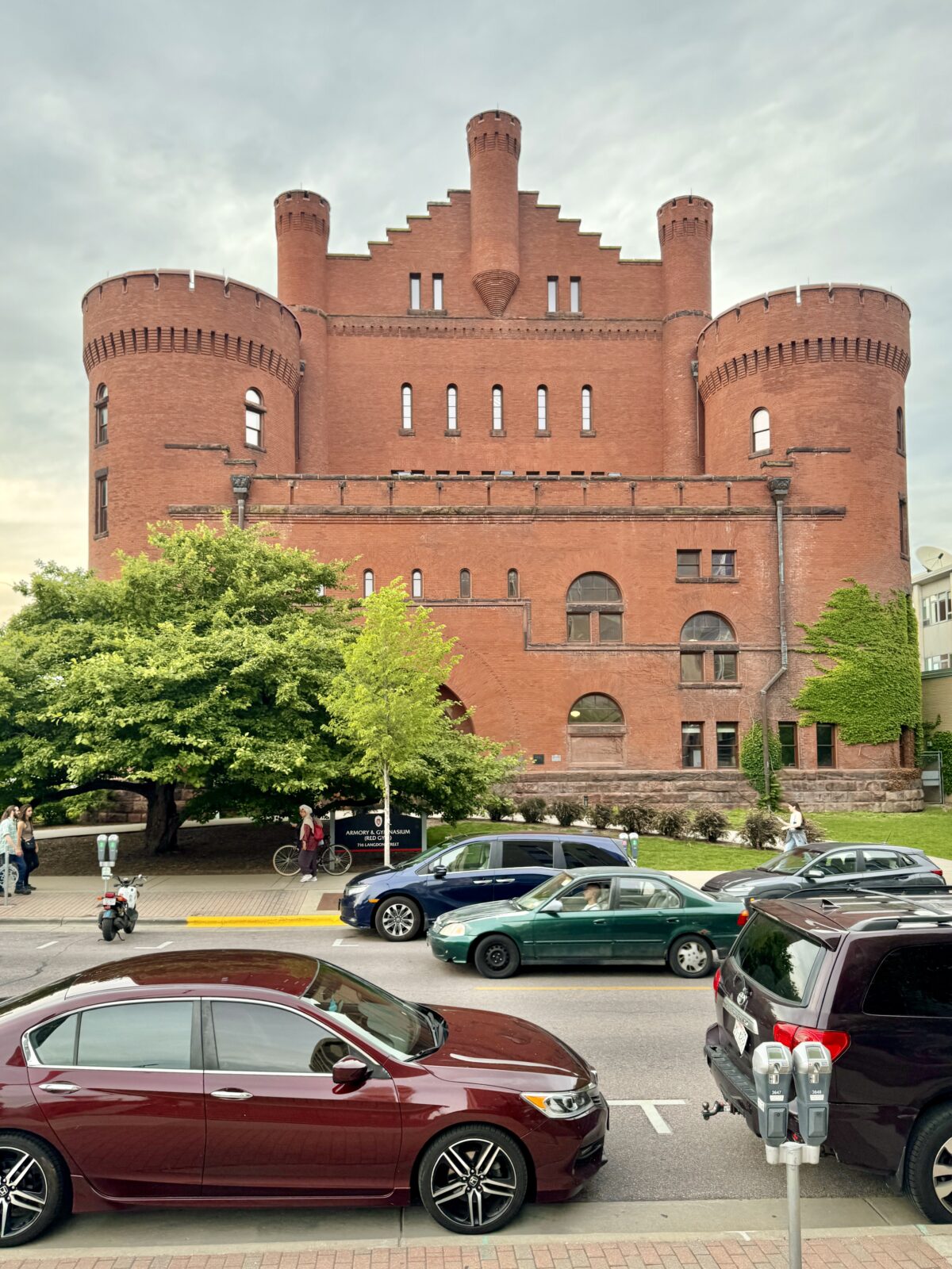 The front of the Red Gym during the daytime with cars parked on the street and people walking by.
