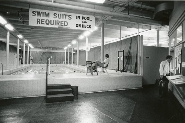 A woman sits in a chair watching a group of swimmers in the Red Gym swimming pool.